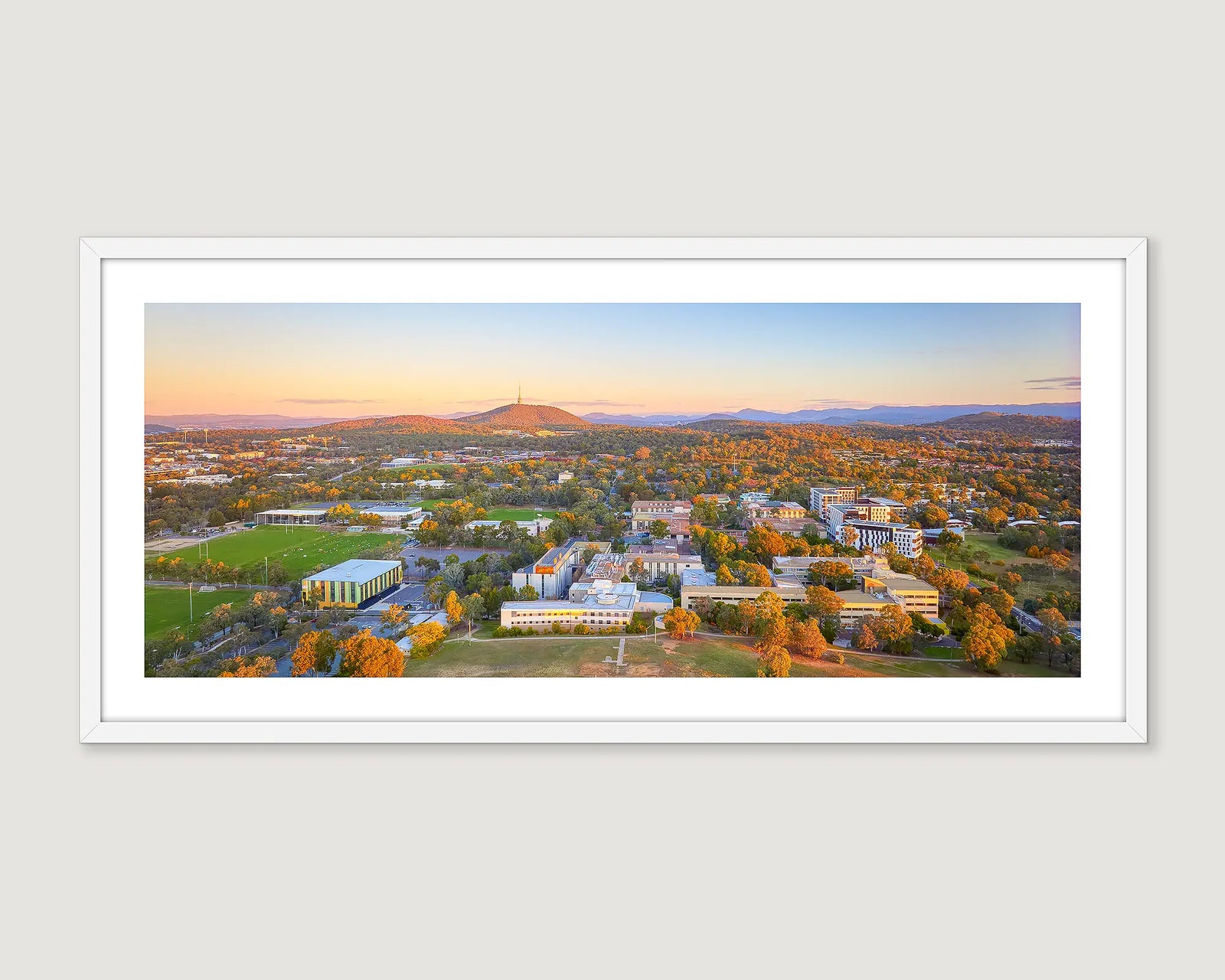 Framed panoramic view of a cityscape and the University of Canberra with buildings and greenery at sunset.
