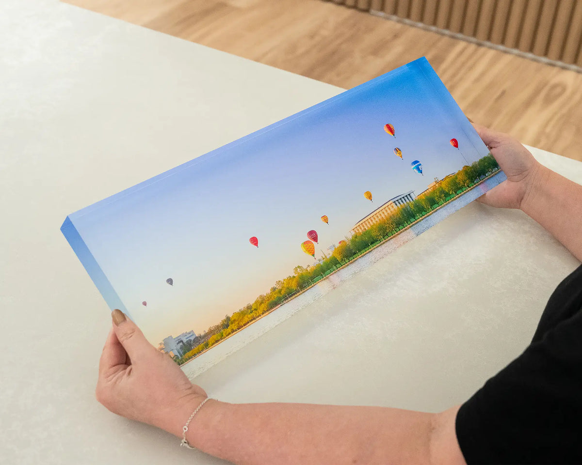 Upwards. Acrylic block of hot air balloons over the National Library of Australia, held in hands.