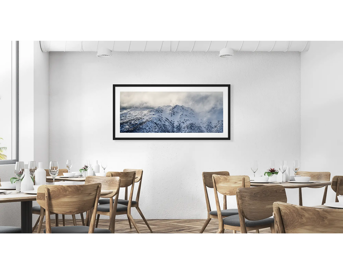 Veil of the Alps. Wall art print of twin humps with fog and snow, framed in a black frame and hung in a cafe. 