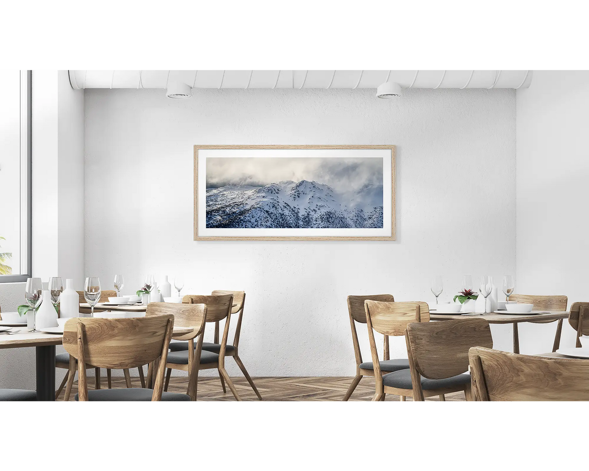 Veil of the Alps. Wall art print of twin humps with fog and snow, framed in a timber frame and hung in a cafe. 