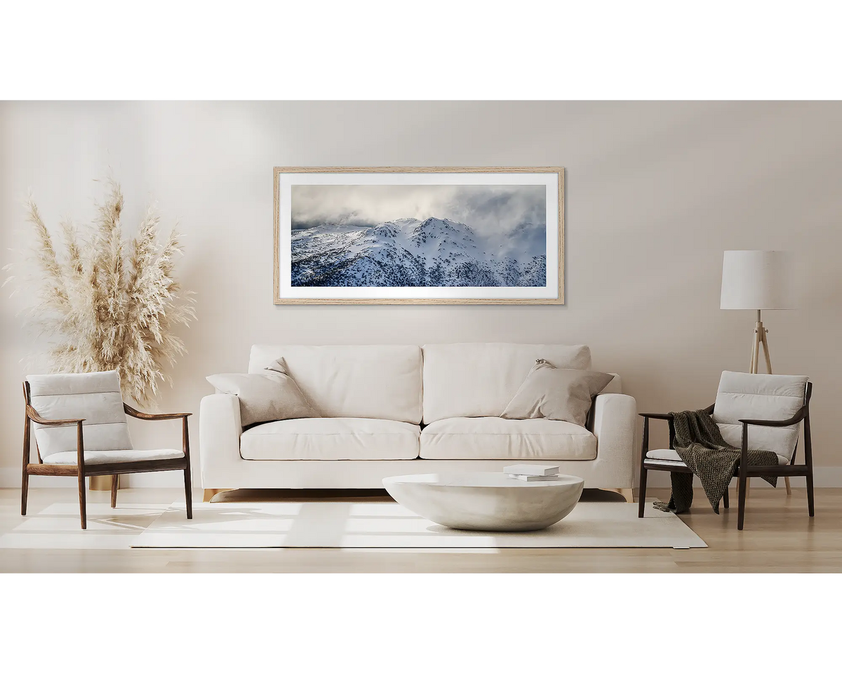Veil of the Alps. Wall art print of twin humps with fog and snow, framed in a timber frame and hung on a wall above a couch. 