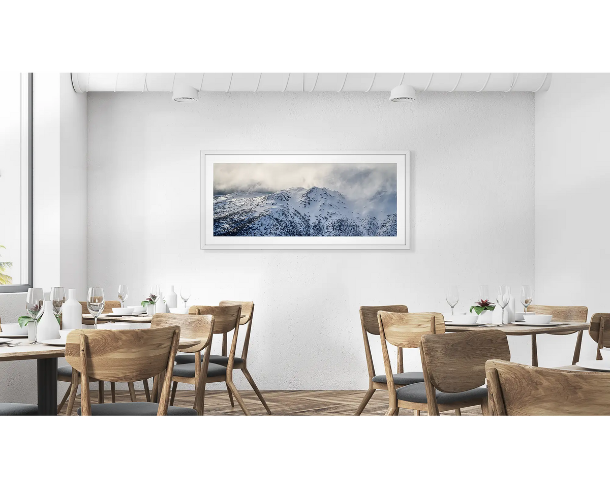 Veil of the Alps. Wall art print of twin humps with fog and snow, framed in a white frame and hung in a cafe. 