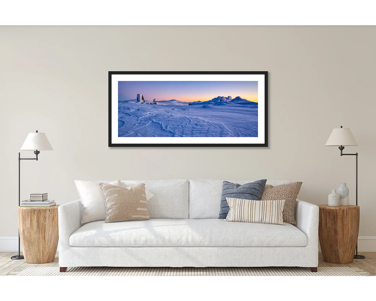 View to Kosciuszko. Wall art print of a snow sunrise, looking to Mount Kosciuszko, framed in a black frame and hung above a couch. 
