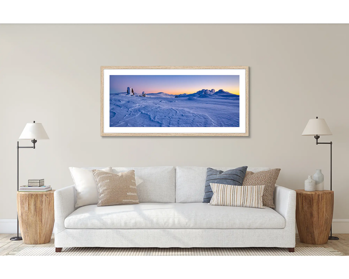 View to Kosciuszko. Wall art print of a snow sunrise, looking to Mount Kosciuszko, framed in a timber frame and hung above a couch. 