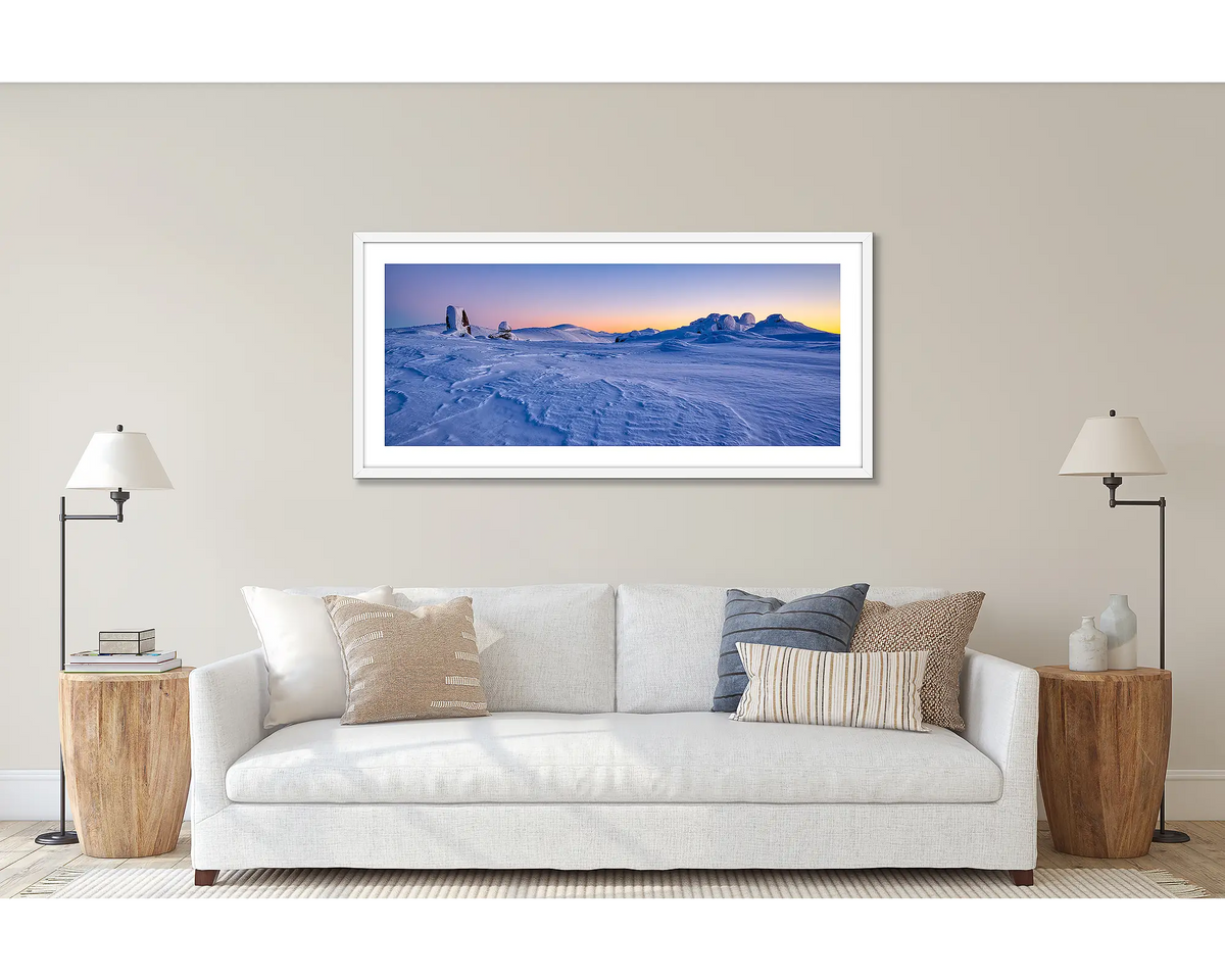 View to Kosciuszko. Wall art print of a snow sunrise, looking to Mount Kosciuszko, framed in a white frame and hung above a couch. 