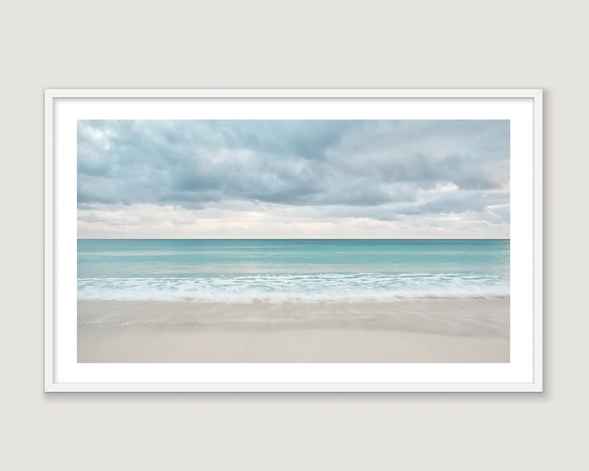 Framed photograph of a turquoise beach and sand and clouds.