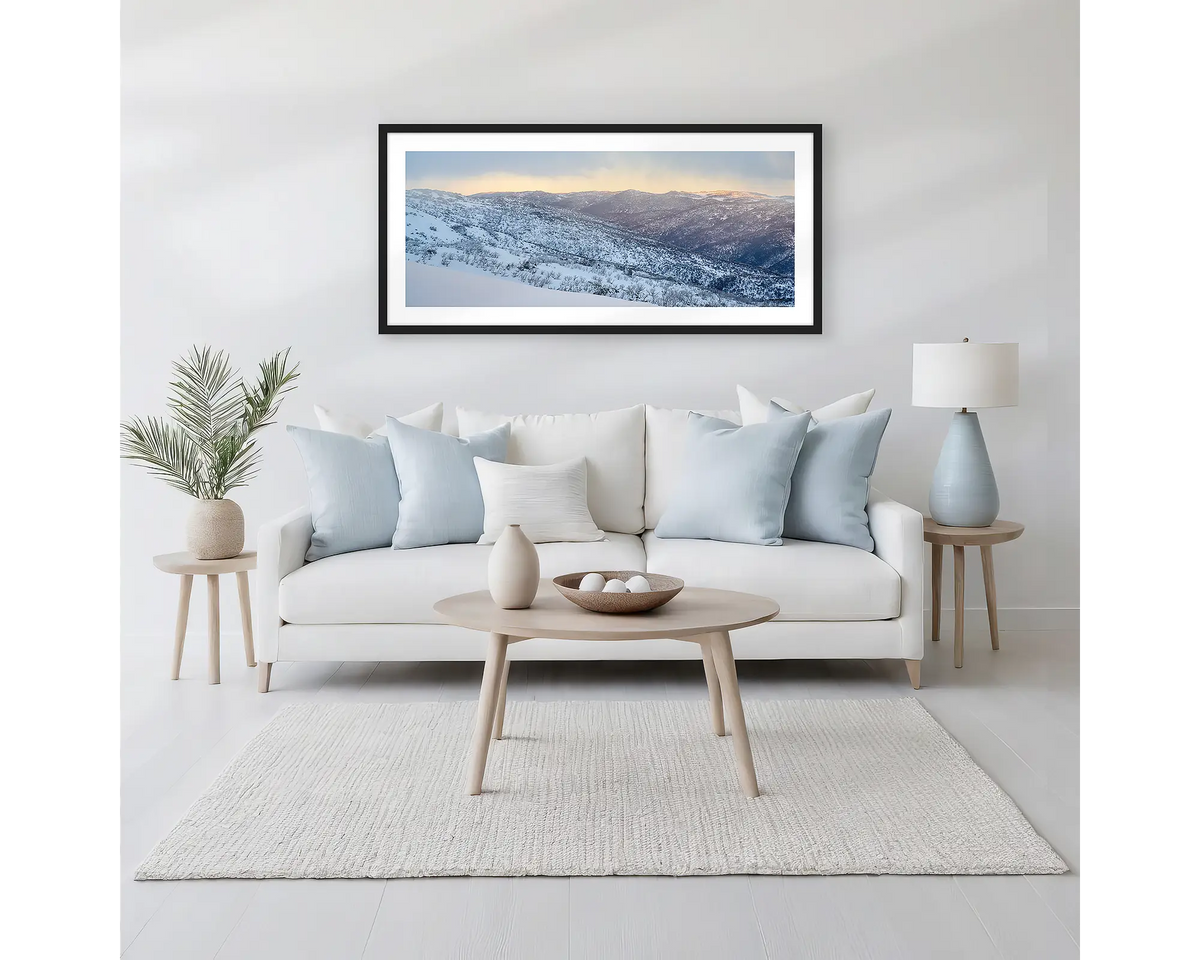 Whispers of Winter. Winter framed wall art print of Thredbo Valley covered in snow, with a black frame hung above a neutral coloured couch. 