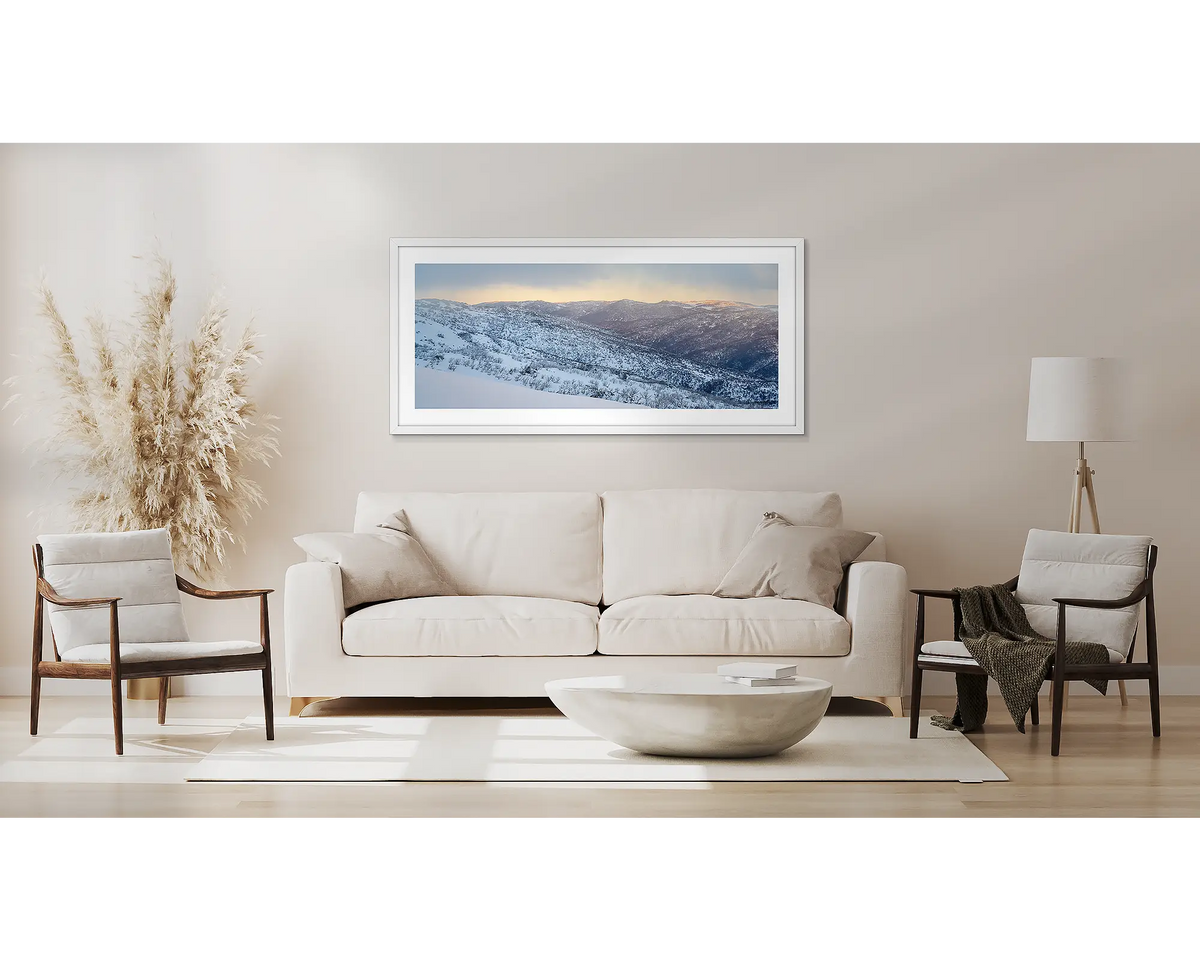 Whispers of Winter. Winter framed wall art print of Thredbo Valley covered in snow, with a white frame hung above a couch. 