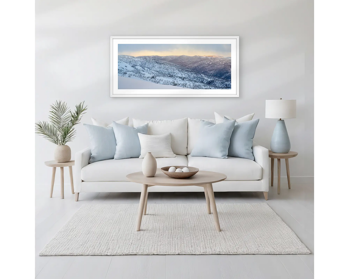 Whispers of Winter. Winter framed wall art print of Thredbo Valley covered in snow, with a white frame hung above a neutral coloured couch. 