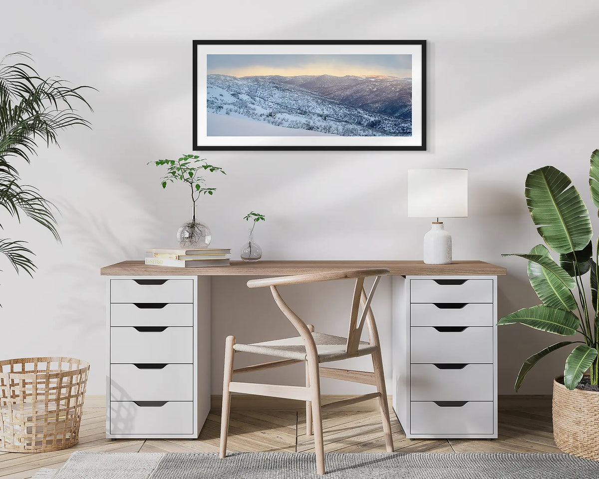 Whispers of Winter. Wall art print of Thredbo Valley covered in snow, framed in a black frame and hung above a small home office desk. 