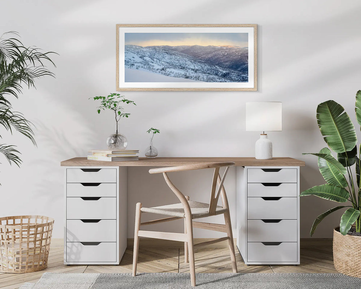 Whispers of Winter. Wall art print of Thredbo Valley covered in snow, framed in a timber frame and hung above a small home office desk. 
