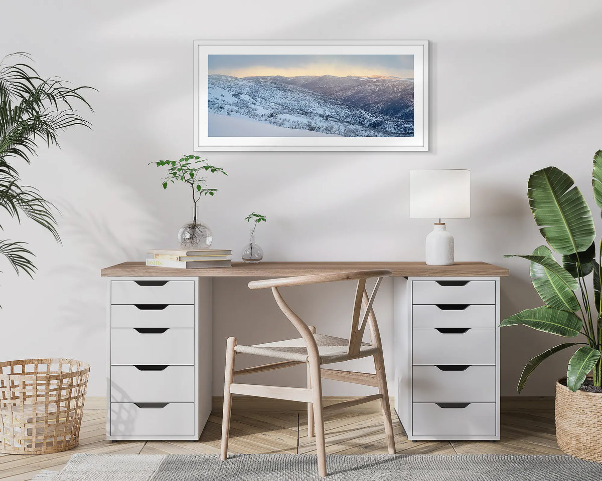 Whispers of Winter. Wall art print of Thredbo Valley covered in snow, framed in a white frame and hung above a small home office desk. 