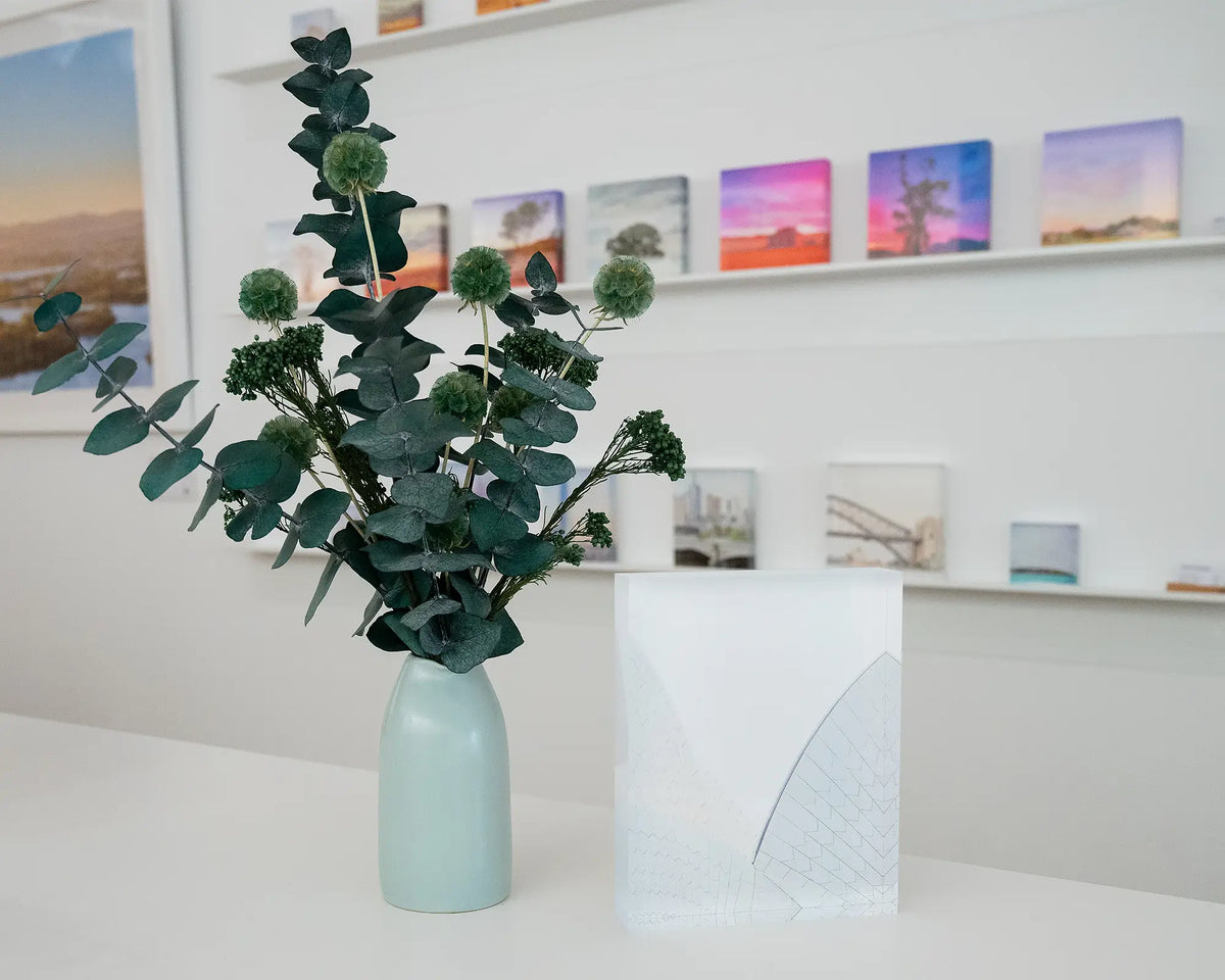 White On White. Acrylic block of the Opera House shells, on gallery desk styled with flower arrangement and acrylic blocks on shelf in background.