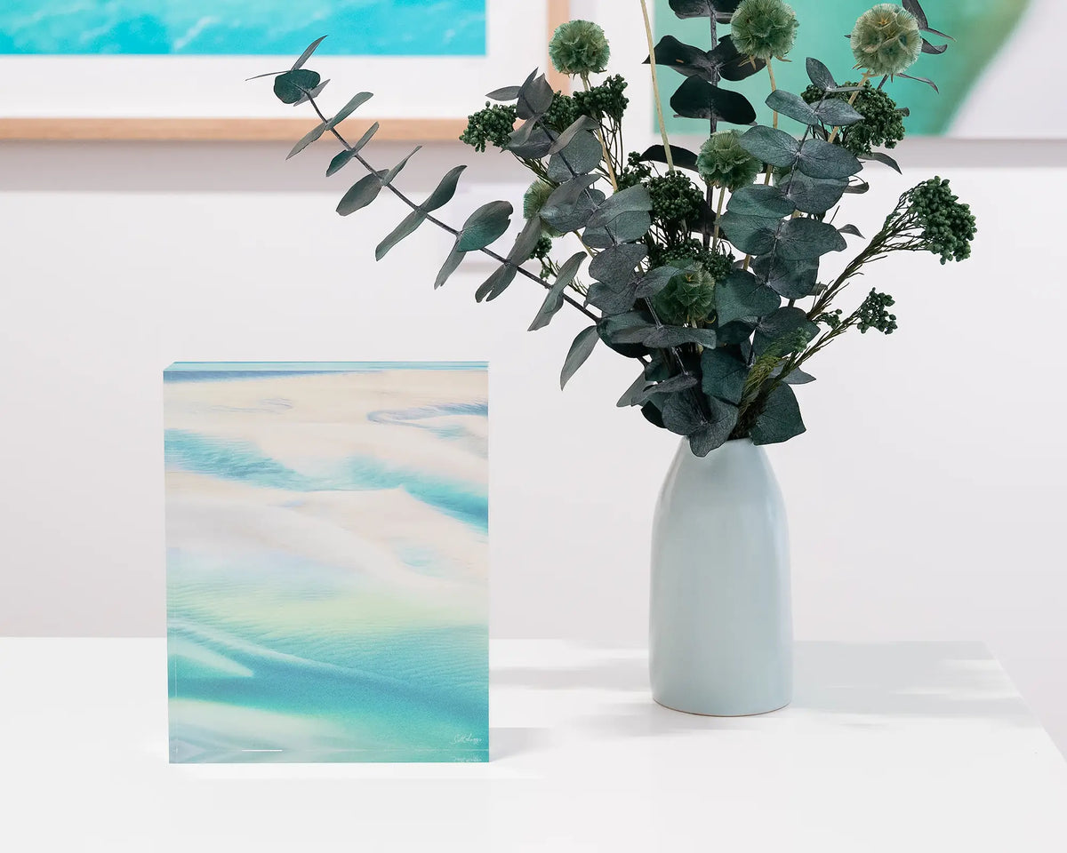 Whitsunday Colours. Acrylic block of an aerial view of Whitsunday Island, Queensland, on desk styled with a small flower vase.