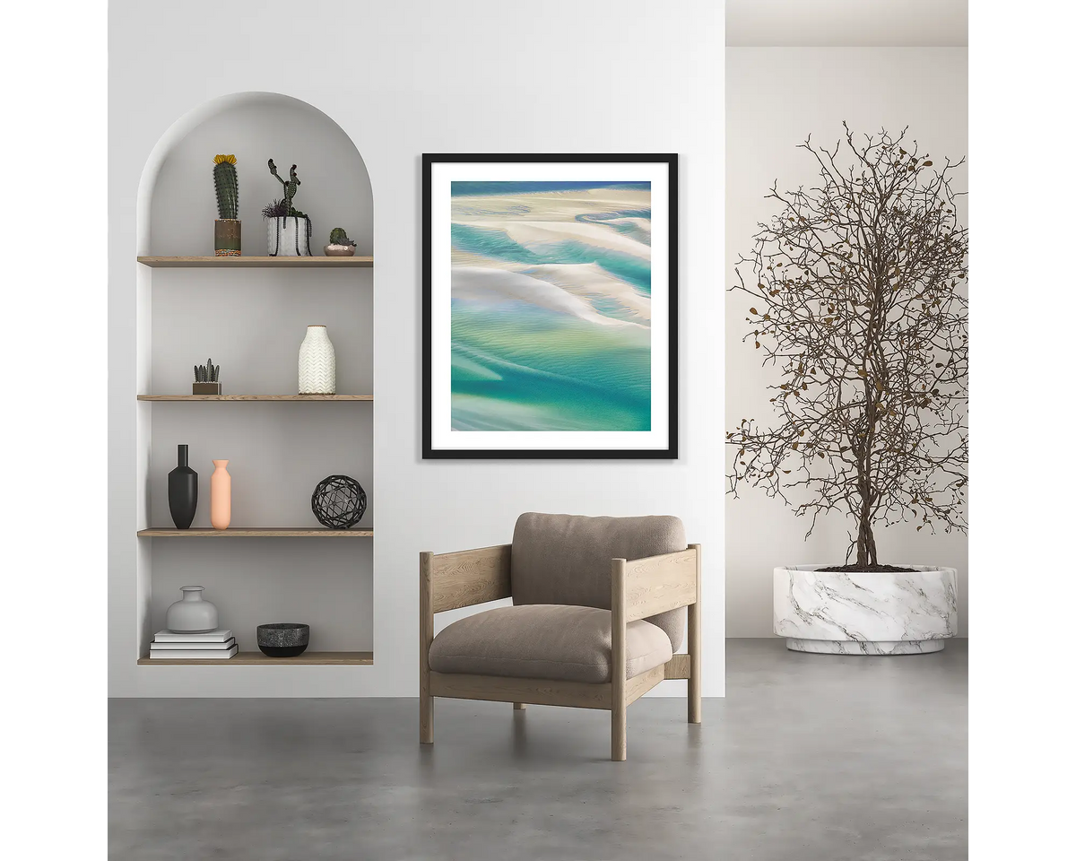 Whitsunday Colours. Coastal wall art print, with a black frame, hung above a chair. 