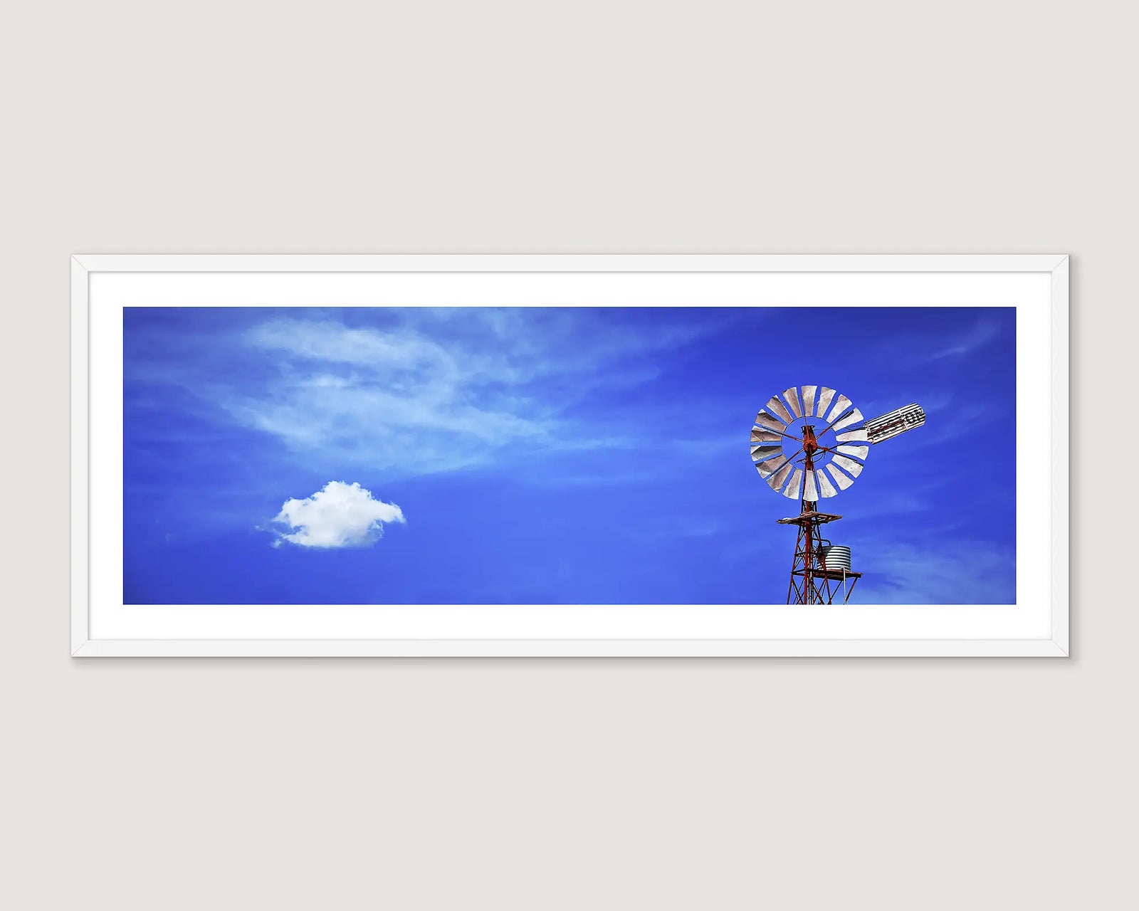 Framed photograph of a windmill with a blue sky and scattered clouds.