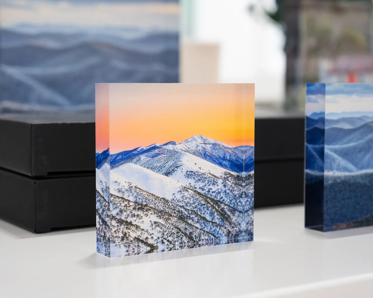 Winter Glow. Acrylic block of an orange sunrise over the summit of Mount Feathertop, on display in gallery with more alpine acrylic blocks.