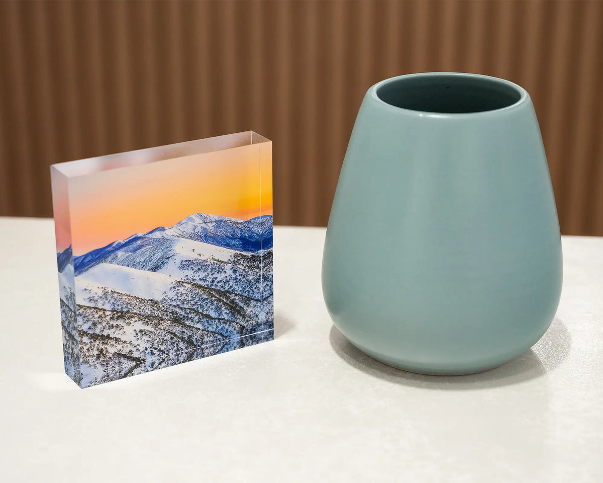 Winter Glow. Acrylic block of an orange sunrise over the summit of Mount Feathertop, styled with a small vase.