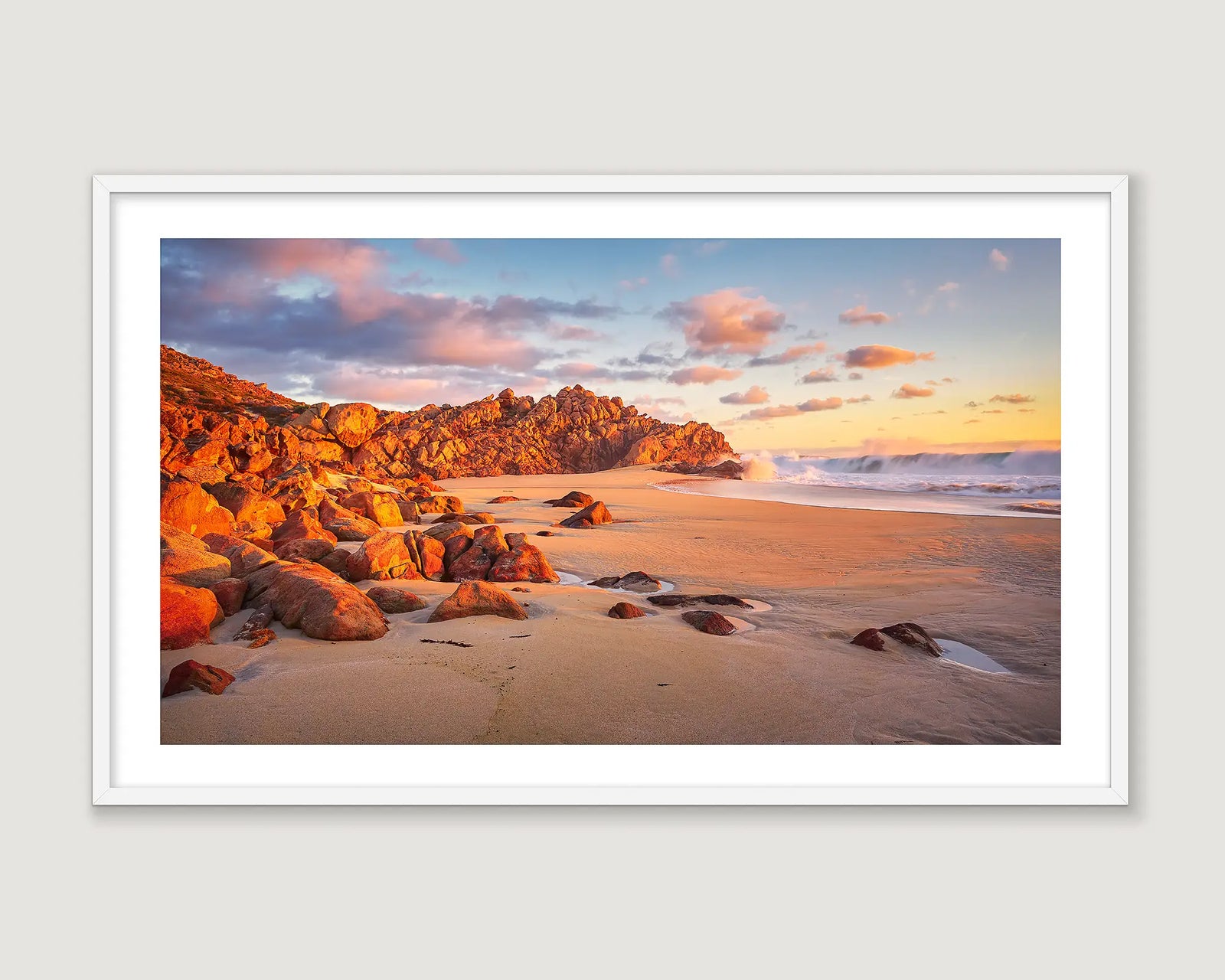 Framed photograph of a rock formation on a beach with scattered clouds and a yellow sunrise.